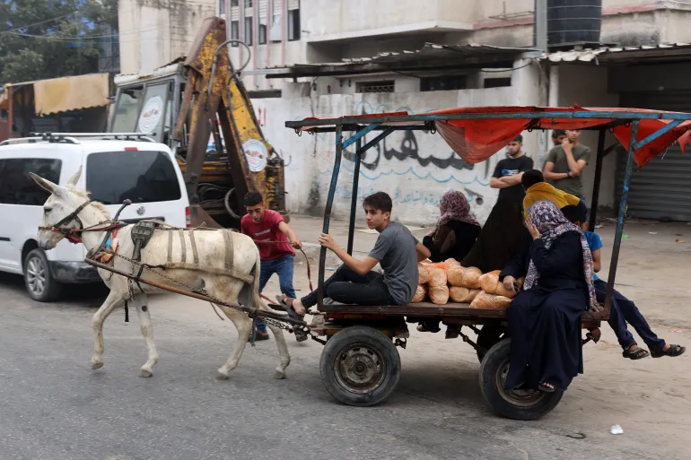 EDITORS NOTE: Contenu graphique / Des personnes transportent du pain en chevauchant un chariot tiré par un âne dans la ville de Gaza le 28 octobre 2023. - Les frappes aériennes israéliennes ont détruit des centaines de bâtiments dans la bande de Gaza pendant la nuit, a déclaré le service de la défense civile du territoire palestinien contrôlé par le Hamas le 28 octobre. (Photo par MOHAMMED ABED / AFP)