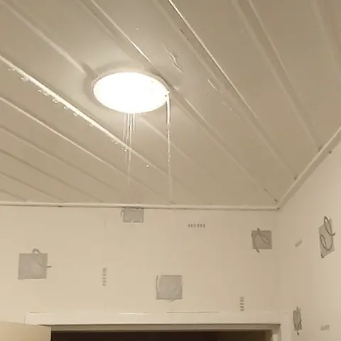 Gros plan sur un luminaire blanc d'où s'écoule de l'eau