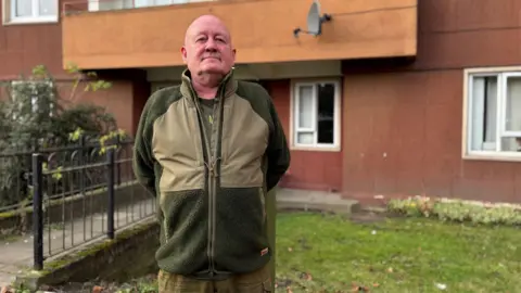 John Butcher debout devant le bâtiment Westfield Court