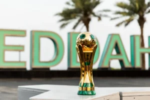 Le trophée doré de la Coupe du Roi d’Arabie saoudite posé devant des palmiers.