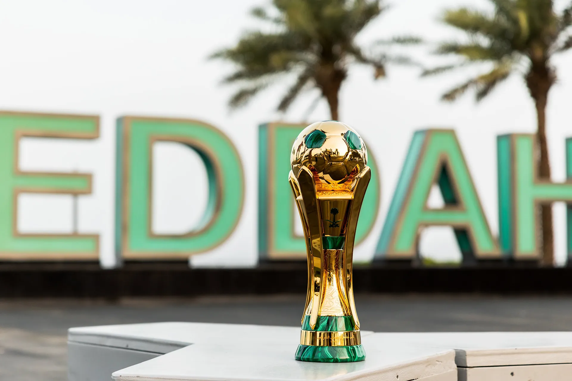 Le trophée doré de la Coupe du Roi d’Arabie saoudite posé devant des palmiers.