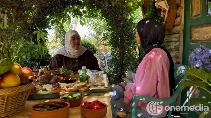 Deux femmes sont assises à une table garnie de produits alimentaires sous une végétation dense.