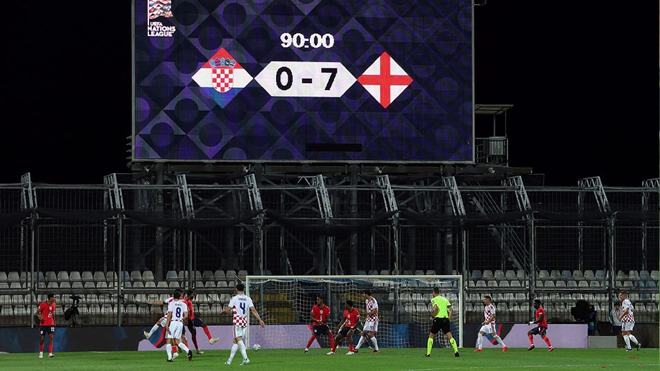 Un panneau de stade affiche 90:00 et le score 0-7 entre les emblèmes croate et anglais, au-dessus de joueurs présents sur le terrain.
