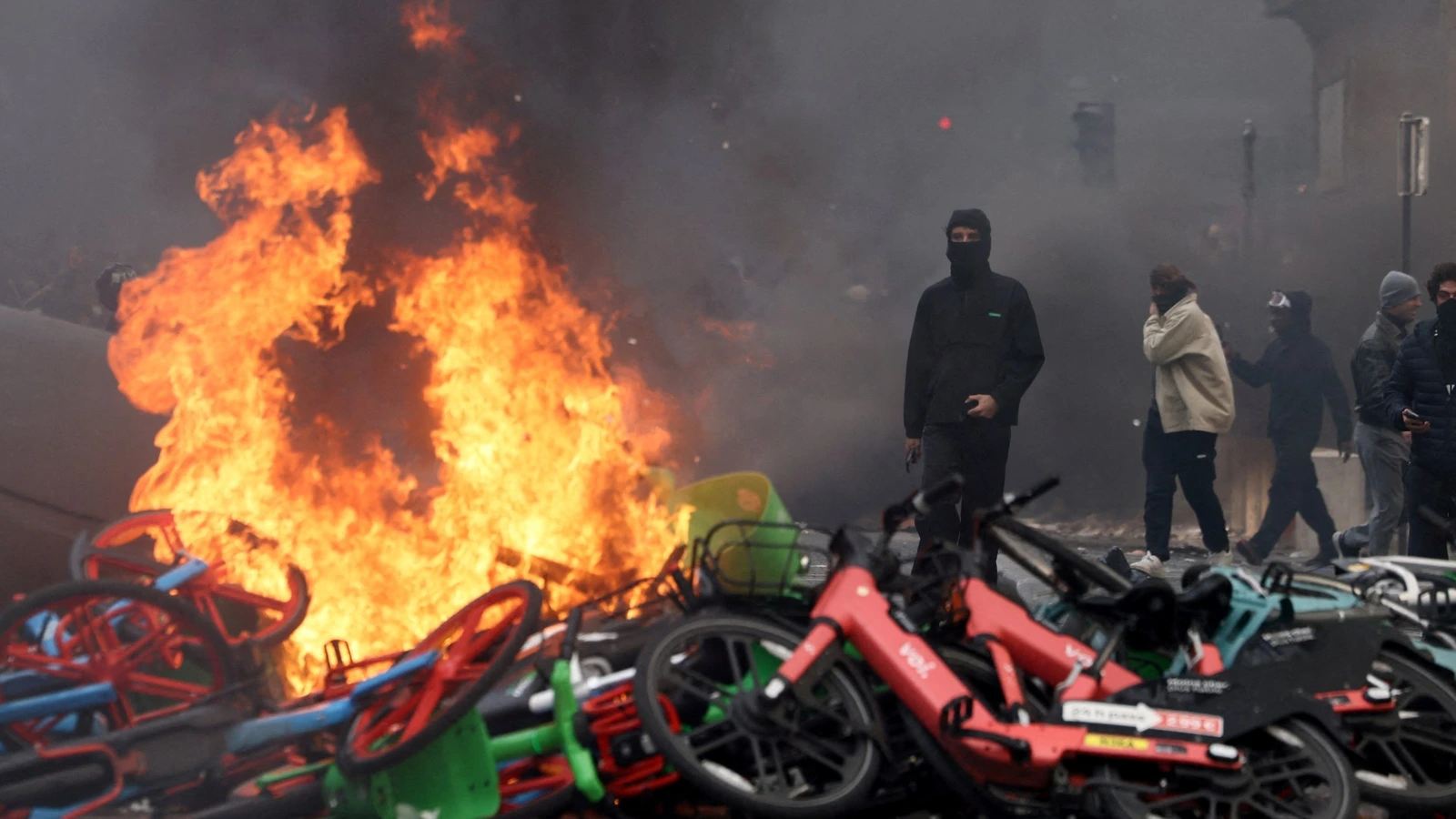 Manifestants masqués près de vélos en feu lors d’une manifestation à Paris.